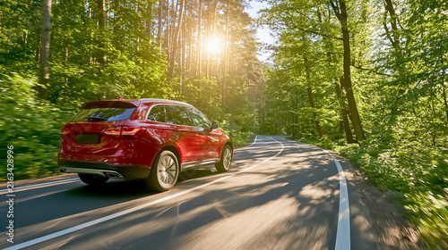 Red SUV driving briskly through a bright green summer forest / travel photo

