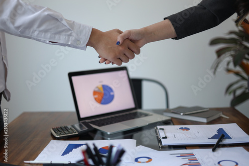 Quadro su tela Businesspeople shaking hands in the meeting over a desk with business documents and laptop for the start or culmination of a professional relationship or negotiation