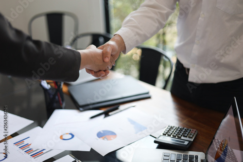 Fotografie Businesspeople shaking hands in the meeting over a desk with business documents and laptop for the start or culmination of a professional relationship or negotiation