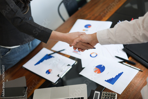 Quadro su tela Businesspeople shaking hands in the meeting over a desk with business documents and laptop for the start or culmination of a professional relationship or negotiation