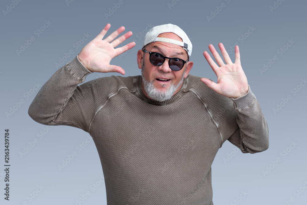 Naklejka premium Excited senior man raises open hands in a cheerful greeting on gray background