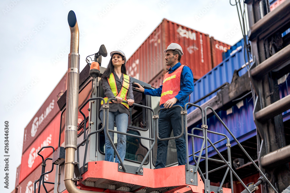 Naklejka premium Worker with a tablet inspects rows of stacked shipping containers at a busy import export freight terminal yard outdoors.