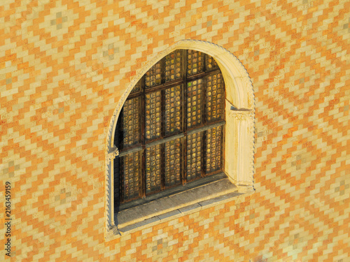 Traditional arched window with ornate metal grating set in geometric patterned orange and yellow wall in Doge's Palace, Venice