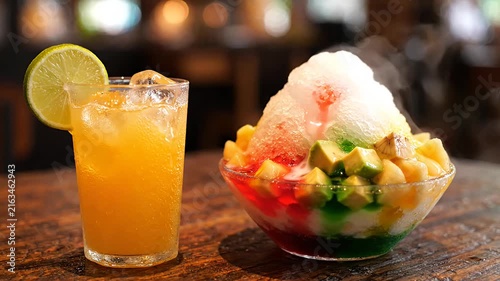 Orange juice and colorful shaved ice dessert on table.