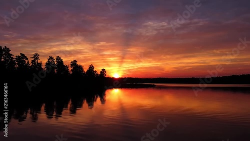 Vibrant sunset over calm lake with forest silhouette.