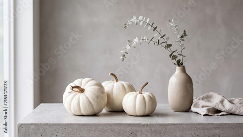 Three white pumkin gourds beside a vase of dried stems on a stone ledge