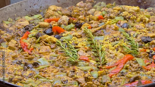 Close up shot of authentic Valencian paella cooking in a large pan with chicken, rabbit, green beans, red pepper and fresh rosemary.
