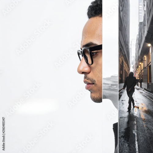 Profile of a young man in glasses looking at a city street reflection in a mirror.