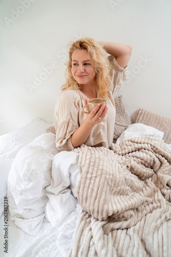 Beautiful blonde woman drinking coffee in her bed in the morning 