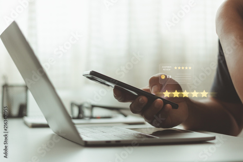 Customer giving online feedback with five star rating and smiley icon on smartphone, concept of customer satisfaction, user experience, service quality, online review , business reputation management.