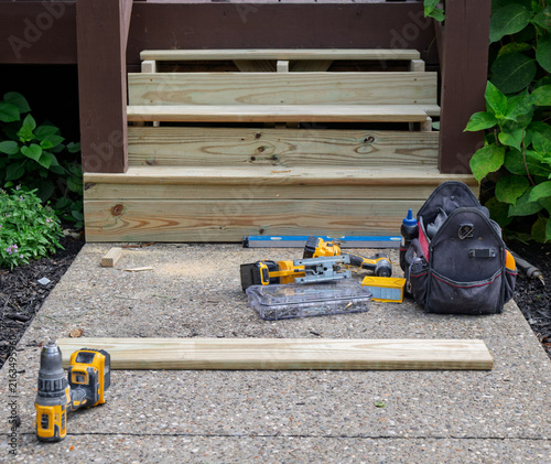 Replacement wooden deck steps rest on a concrete walkway.