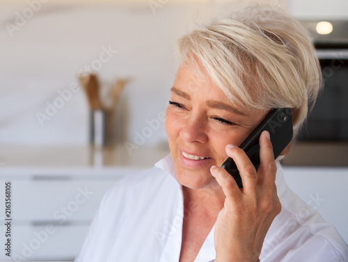 Attractive mature woman smiling listening on cell phone while in kitchen.