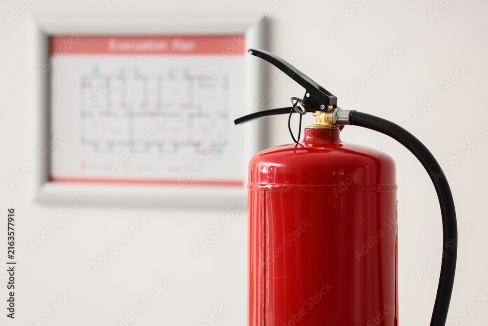 Obraz premium Fire safety and emergency preparedness, red fire extinguisher with an evacuation plan in the background