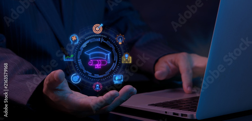 Quadro su tela Businessman using laptop computer while open hand supporting glowing graduation cap education circle nodes
