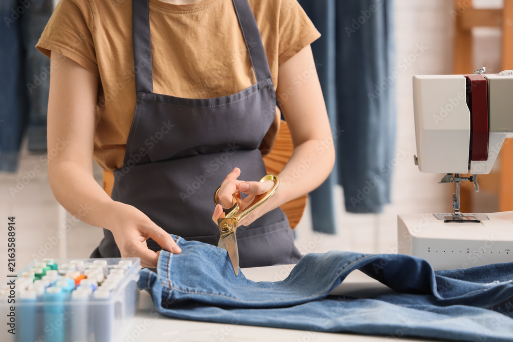 Fototapeta premium Sustainable fashion and upcycling, woman cutting denim with scissors for clothing repair and textile reuse