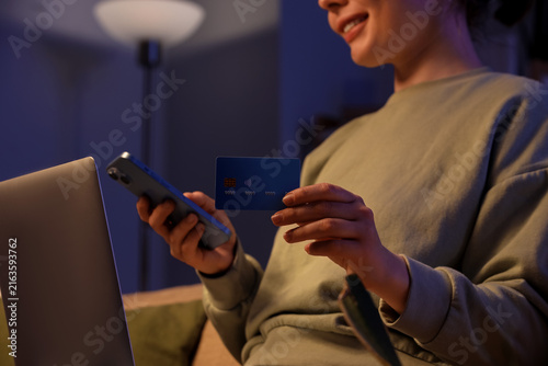 Young happy woman with credit card and mobile phone using laptop for online s...