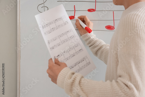 Teenage boy writing music notes on whiteboard in classroom, closeup