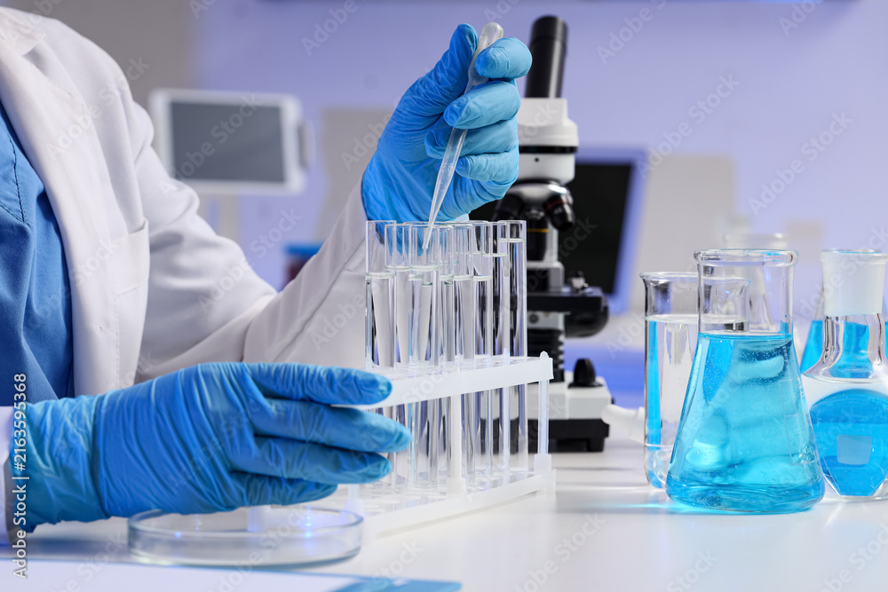 Fototapeta premium Female scientist dropping water sample into test tube at table in laboratory, closeup