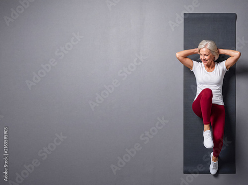 Energetic senior woman performing bicycle crunches on a yoga mat, captured from a top-down view for fitness.