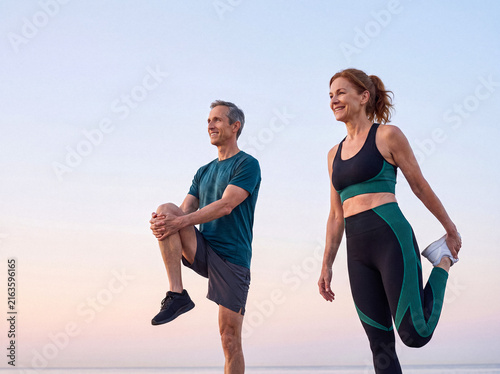 Happy middle-aged couple stretching outdoors, enjoying an active lifestyle and morning exercise together on the beach.