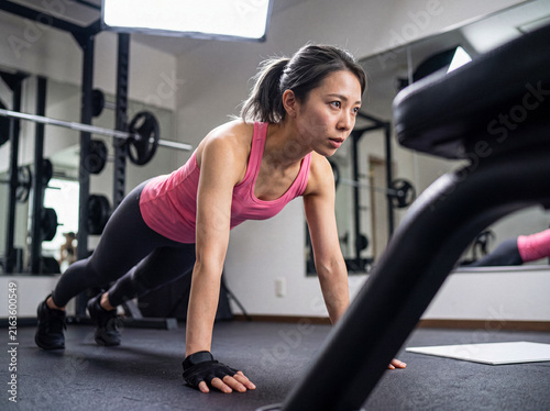 Cuadro en lienzo Focused young Asian woman performing intense push-ups during a challenging strength training workout in a modern gym