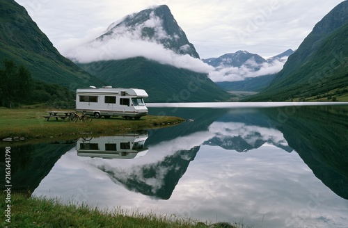 Recreational vehicle parked by calm lake amidst misty mountains