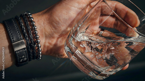 Close-up shot of a hand holding an empty cocktail or whiskey glass against a dark background
