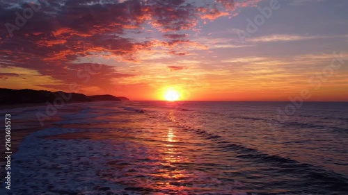 Vivid sunset over the ocean horizon with glowing orange clouds and gentle coastal waves at dusk