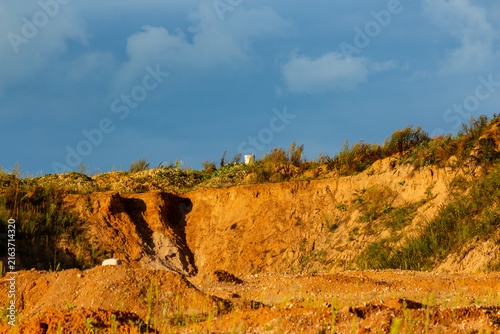 Fotografie Golden textured earth of a rugged clay quarry ridge under a vibrant blue sky wit