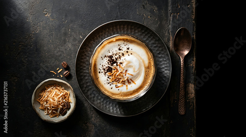 Creamy Coconut Latte Coffee Served in a Dark Ceramic Bowl with Toasted Coconut Flakes and Grated Chocolate Topping