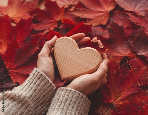 Hands Holding Wooden Heart on Autumn Leaves