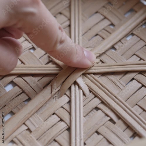 Close-up of a finger pressing down on intricately woven rattan basket detail, showcasing traditional handicraft.
