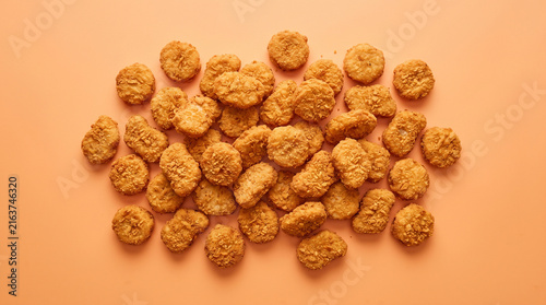 Top view of crispy golden chicken nuggets pile on solid orange background