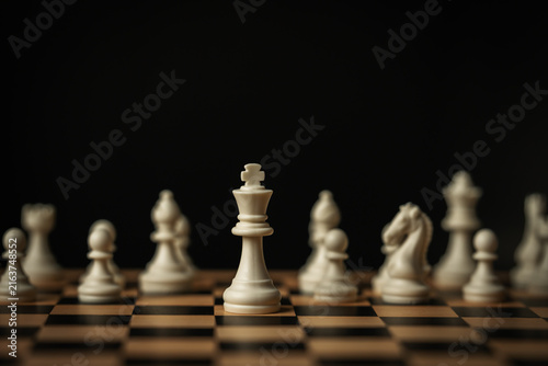 Fotografie white chess king standing tall on a board, surrounded by blurred pieces on black
