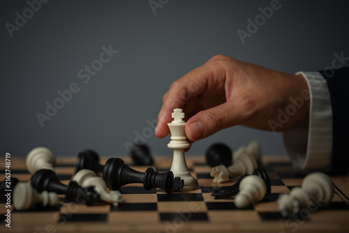 Fotografie business hand holding white chess king on board with fallen pieces