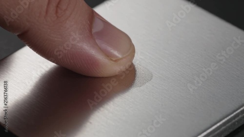 Close-up of a finger gently touching a brushed aluminum surface, highlighting its texture and metallic sheen