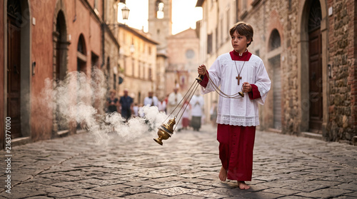 Barefoot altar boy swinging a thurible with incense smoke during a procession