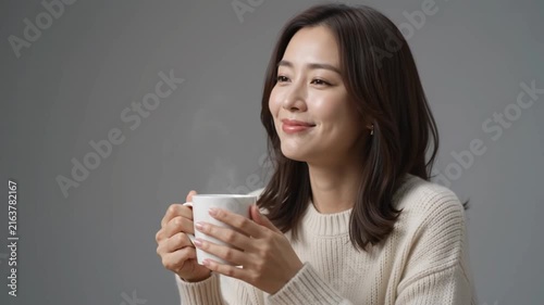 Asian woman in white sweater drinking hot coffee at a table