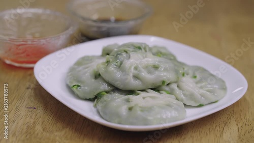 Steamed Chinese chive dumplings served on a white plate with dipping sauces on a wooden table. Traditional Asian snack known as Kuichai, featuring translucent dough and green vegetable filling.