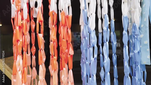 Colorful vertical streamers made of orange, white and blue plastic ribbons hanging outdoors. Decorative chain link ornaments for festive events, celebrations or street festivals. Close up view.