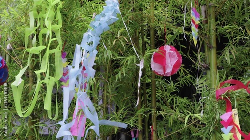 Japanese Tanabata Star Festival decorations hanging on lush green bamboo branches. Features colorful paper streamers, handmade ornaments, and wishing tags in a vibrant outdoor summer display.