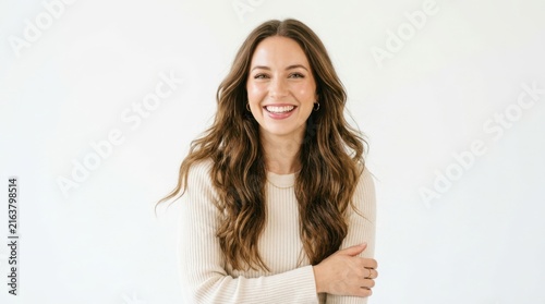 Happy young woman with long wavy brown hair smiling and looking at camera wearing a casual beige sweater in a portrait