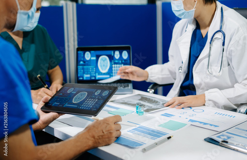 Healthcare team wearing face masks review clinical reports, brain scans, and digital medical charts during a collaborative neurology consultation