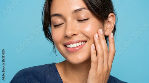 Close up smiling woman touching cheek with healthy skin blue background