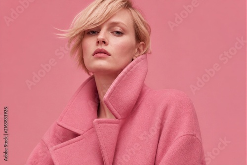 Blonde woman posing in oversized pink coat studio backdrop