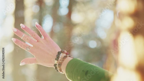 Hand reaches toward warm sunlight through forest. Fingers gently open, catching golden rays. Soft focus on blurred trees behind. Calm, peaceful, hopeful moment captured. Ideal for wellness, meditation
