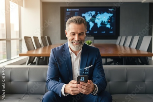 Businessman using smartphone in modern office, confident male professional with lanyard, corporate waiting lounge