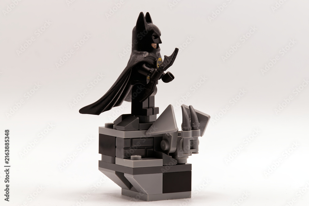 Fototapeta premium Bologna - Italy - August 19, 2026: Lego batman minifigure standing on a grey stone gargoyle ledge holding a batarang weapon.