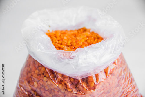 A close-up food shot showing vibrant, raw red lentils packed tightly inside a clear plastic bag, clean white background. selective focus, taken in a studio with artificial direct light at Cairo Egypt