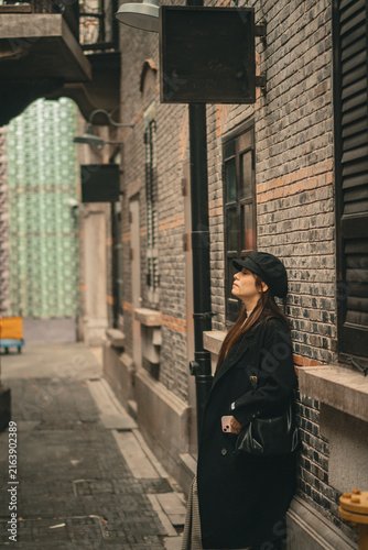 Photography Woman leaning against brick wall under vintage shop sign, Xintiandi, Shanghai